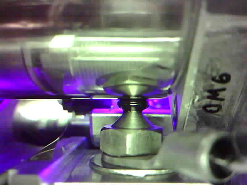 Onboard printer camera view: resin extruded and cured under ultraviolet light, casting a violet glow across a freshly printed structure in orbit.